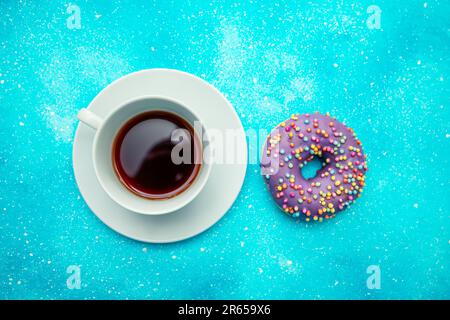 Lilac donut and a cup of coffee on a blue background. Stock Photo