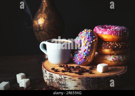 Stack of assorted donuts and a cup of coffee on a dark background. Stock Photo