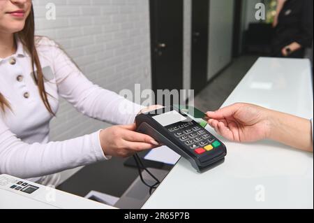 Customer's hand pays by credit card and NFC technology, entering pin code on reader holded by manager at reception desk Stock Photo