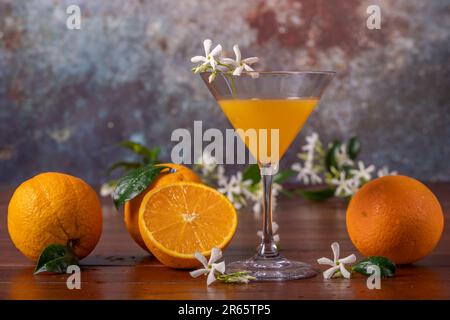 A glass decorated with white flowers contains orange juice, with whole and halved oranges next to it Stock Photo