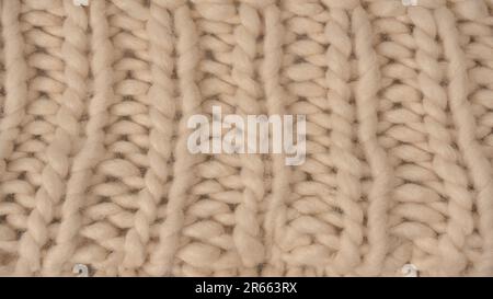 A fragment of beige knitted fabric, knitted from white sheep wool. Knitted background. Stock Photo