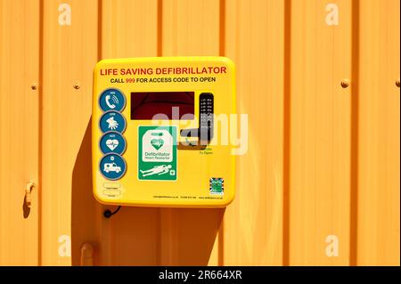 Life saving yellow defibrillator in box mounted on orange wall Stock Photo