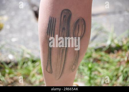 Close up of a tattoo featuring cutlery on a man's calf Stock Photo