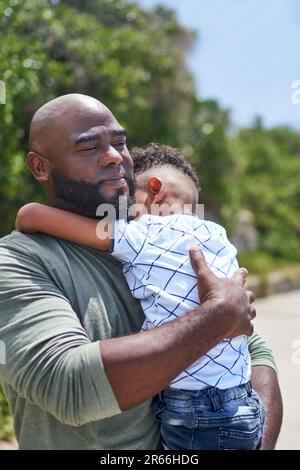Affectionate father holding tired son on sunny footpath Stock Photo