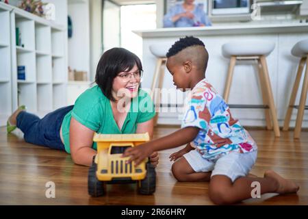 Happy mother and son playing with toy dump truck on floor at home Stock Photo