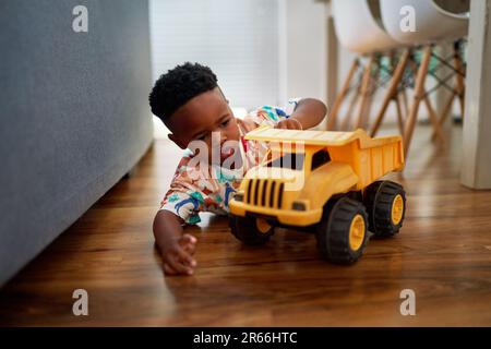 Cute boy playing with dump truck on hardwood floor at home Stock Photo