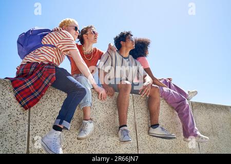 Young couple friends hanging out, sitting on sunny ledge Stock Photo