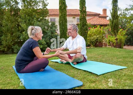 Happy senior couple holding hands on yoga mats in villa garden Stock Photo