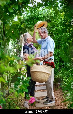 Happy senior couple with flowers under trellis in summer garden Stock Photo