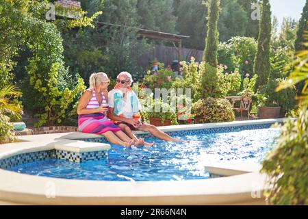 Happy senior couple relaxing, drinking cocktails at sunny swimming pool Stock Photo