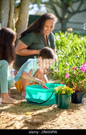 Family planting flowers in sunny summer garden Stock Photo