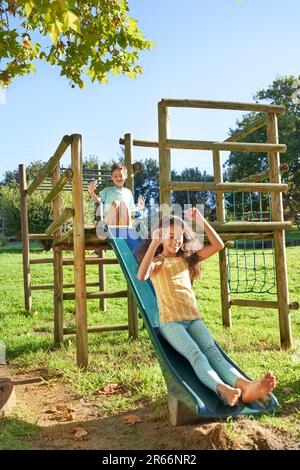 Carefree brother and sister playing on slide at playground structure Stock Photo