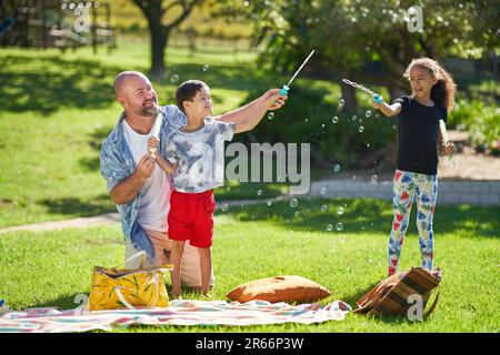 Happy family playing with bubbles in sunny summer park Stock Photo