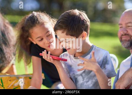 Sister watching brother with Down Syndrome using smart phone in park Stock Photo