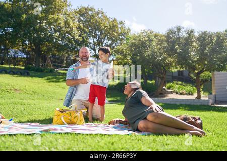 Happy family relaxing and playing with bubbles in sunny summer park Stock Photo