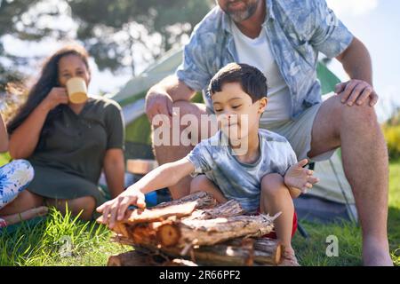Father watching son with Down Syndrome stacking firewood at campsite Stock Photo
