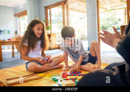 Sister and brother with Down Syndrome playing with toys on floor Stock Photo