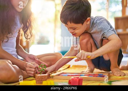 Sister watching brother with Down Syndrome playing with toys on floor Stock Photo