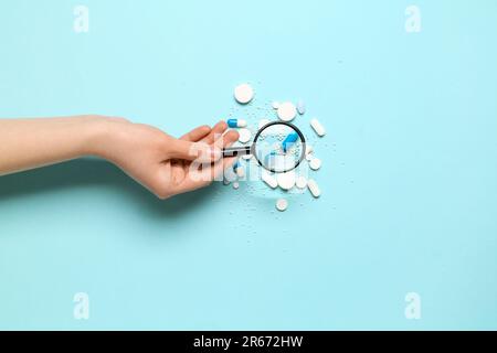 Female hand with magnifier and pills on blue background Stock Photo