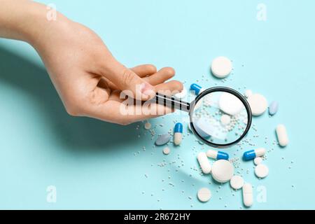 Female hand with magnifier and pills on blue background Stock Photo