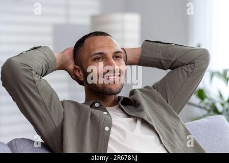 Portrait of a satisfied African American businessman, freelancer man sitting at home with his hands behind his head on the couch and resting after a h Stock Photo