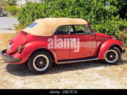 Shiny red well-kept VW Beetle convertible motor car with beige roof parked by the roadside, Agistri island, Saronic Gulf, Greece. May 2023. Stock Photo