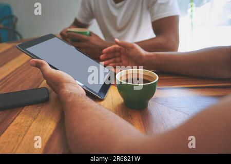 Coffee inspires us to create. two unrecognizable friends sitting together and using a tablet during a discussion in a coffeeshop. Stock Photo