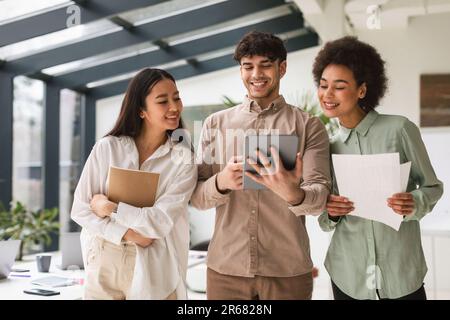 Three Young Multiracial Colleagues Using Tablet Computer Together In Office Stock Photo