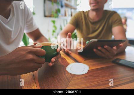 Fueled by coffee and great ideas. two unrecognizable friends sitting together and using a tablet during a discussion in a coffeeshop. Stock Photo
