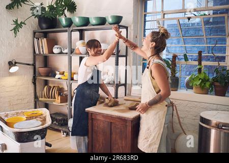 A friend in art is a friend of the heart. two young women giving each other a high five in a pottery studio. Stock Photo