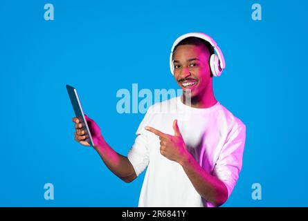 Positive black guy pointing at digital tablet, using headphones Stock Photo
