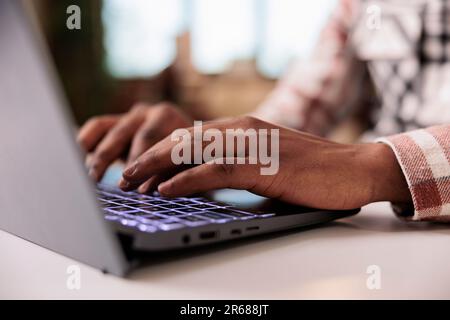 Closeup of male programmer writing code on laptop keyboard while working remote from home living room. Selective focus on african american hands typing and coding software on portable computer. Stock Photo