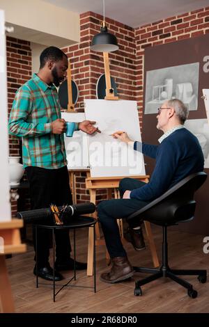 Senior man attending art classes interacting with other students and teachers during drawing lesson, people learning something new in retirement. Creative team building activities Stock Photo