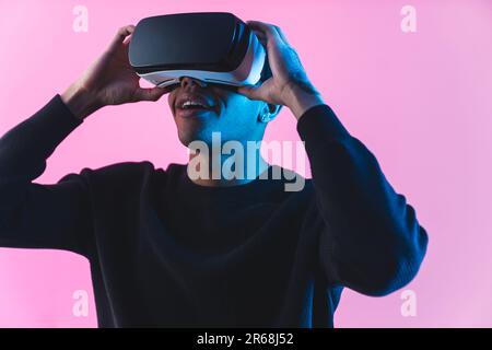 Astonished black male model wearing a VR headset watching videos. Studio shot isolated against a pink background. High quality 4k footage Stock Photo