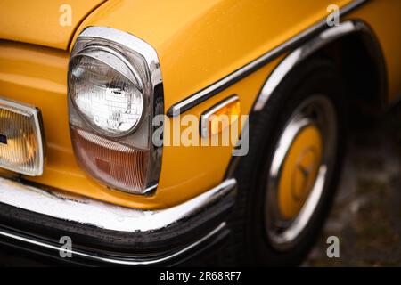 Izmir, Turkey - June 3, 2023: Close-up shot of the headlight on a yellow 1970 Mercedes, covered in raindrops, at the IZKOD Classic Car Meet at Buca Po Stock Photo