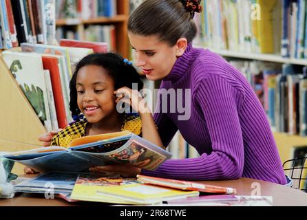 Caucasian librarian Reading with an African-American elementary school student in the school library Stock Photo