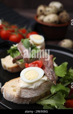 Delicious bruschettas with anchovies, cream cheese, arugula, eggs and tomatoes on table, closeup Stock Photo