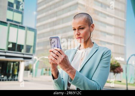 Serious business woman watching news on the cellphone. Successful businesswoman standing at workplace using a mobile phone to read e-mails. Corporate female holding a smartphone and texting on a app. High quality photo Stock Photo