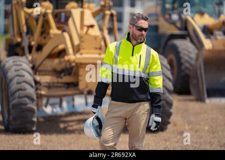 Excavator loader tractor and buider worker. Construction man with helmet. Worker at construction new building. Builder at construction site. Foreman w Stock Photo