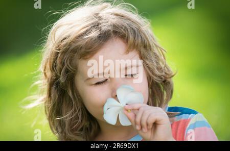 Close up face of cute child outdoors. Funny child smelling plumeria flower. Dreamy kids face. Daydreamer child portrait close up. Dreams and Stock Photo