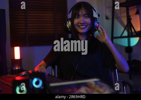 Female cyber hacker gamer in headphone playing games or hacking programming system in neon light. Stock Photo