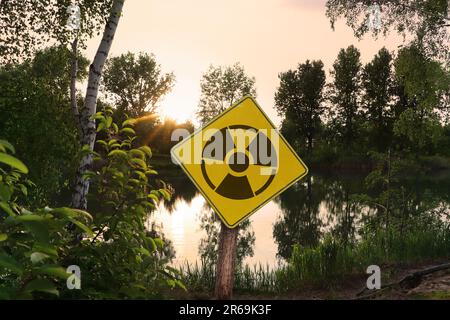 Radioactive pollution. Yellow warning sign with hazard symbol near contaminated area outdoors Stock Photo