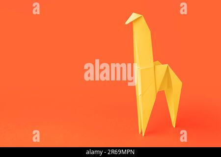 Origami art. Handmade yellow paper giraffe on orange background, space for text Stock Photo