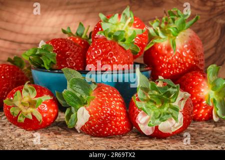 Fresh strawberries with water drops in a blue bowl on a wooden table natural sunlight, selective focus, strawberry spring season Stock Photo