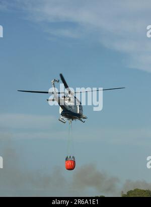 A helicopter takes flight that collaborates in the extinction of a nearby fire carrying water from a canal with the Bambi bucket system Stock Photo