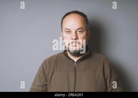 middle aged man in his 40s with short dark hair and graying beard against gray wall with copy space Stock Photo