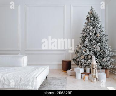 Studio decorations with stylish decorated Christmas tree with presents, toys, nutcracker in big white spacious living room with modern interior, sofa Stock Photo