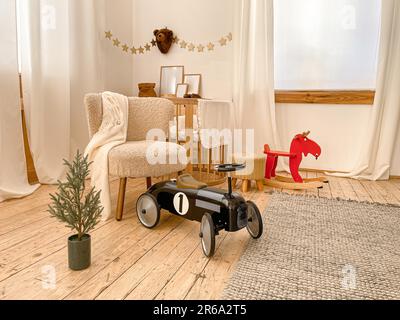 Stylish spacious Scandinavian newborn baby nursery room with toys, bed, playpen, chair, wooden rocking horse, car. Modern interior with beige light Stock Photo