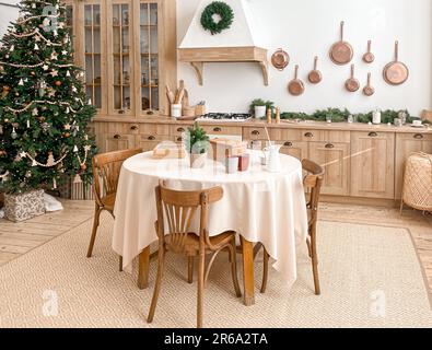 Modern, light, festive, cozy kitchen interior with Christmas and New Year decorations, kitchen table, utensils, copper pans on wall and big Christmas Stock Photo