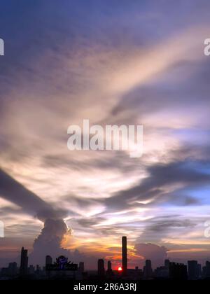 Vertical image, Sunset in the evening with dramatic shape and color of clouds and sky with Silhouette of cityscape, building skyline, nature backgroun Stock Photo